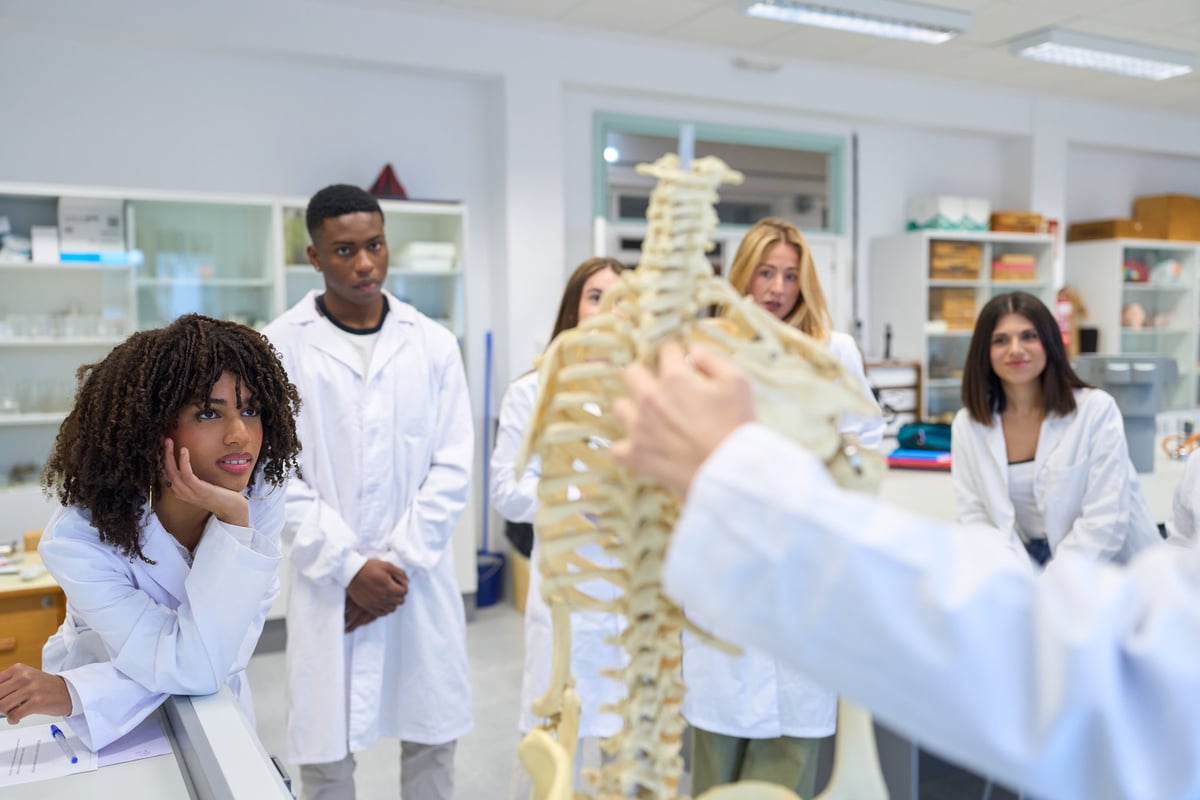 Group of high school students learning anatomy with a human skeleton model during a biology lesson in the school laboratory